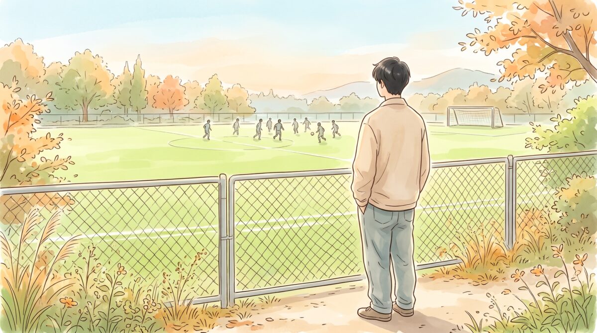 朝の練習場のフェンスの外から、遠くで練習する人たちを見つめる男性の後ろ姿